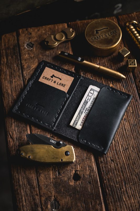Black leather wallet with cash, a brass pen and a knife on wood