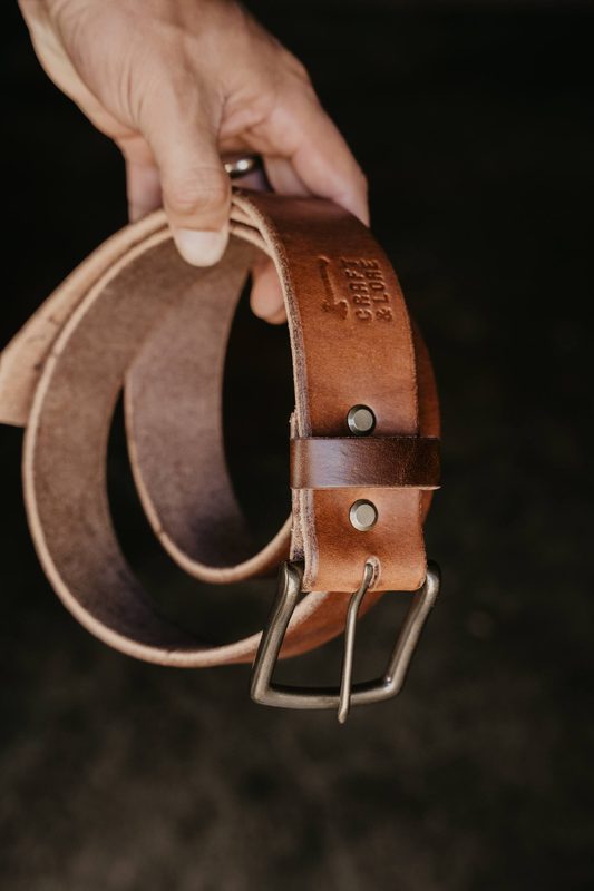 Hand holding a coiled brown leather belt with a steel buckle