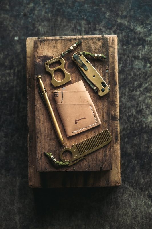 Leather card wallet with a brass pen, comb and bottle opener on a wood block
