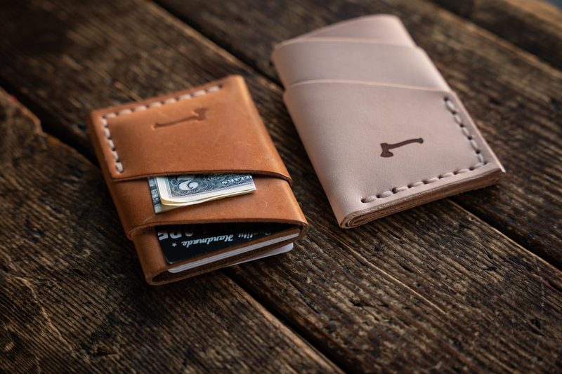 Two leather card wallets, one tan and one natural, on weathered wood