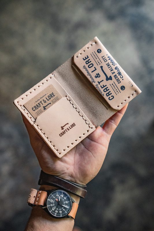 Hand holding a natural leather wallet stamped with the Craft & Lore mark