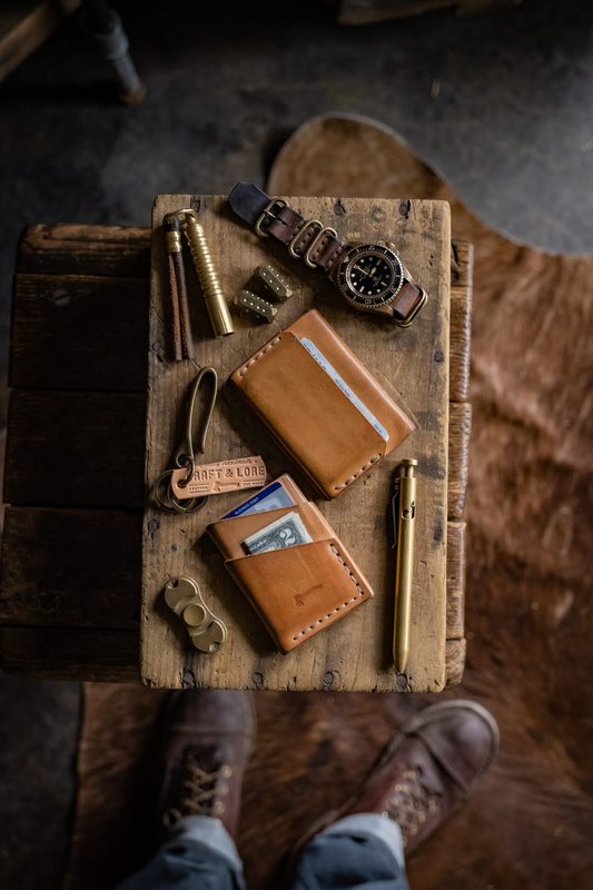 Leather card wallets and brass tools on a wood block, boots below