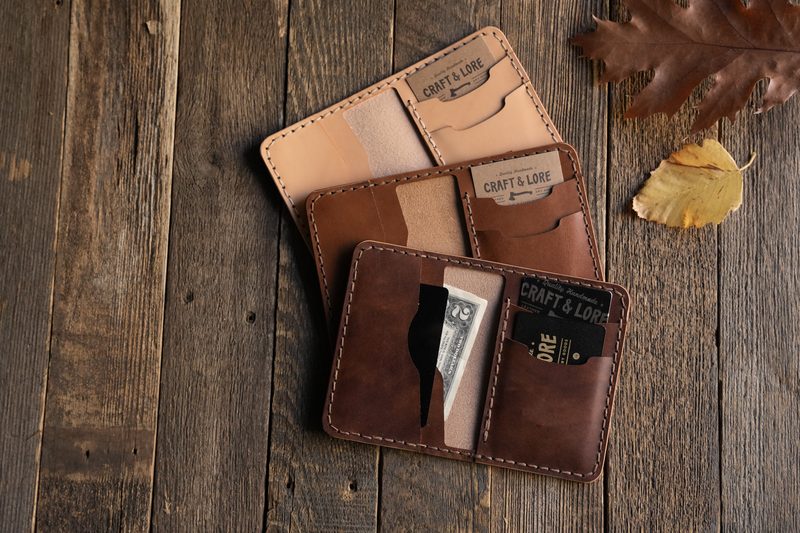 Three handmade leather wallets on barnwood with an autumn leaf