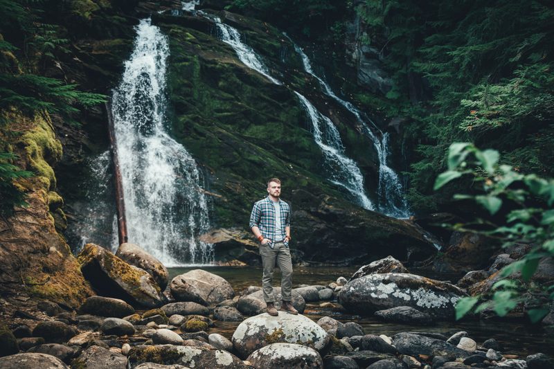 Small figure standing below a waterfall in a mossy forest