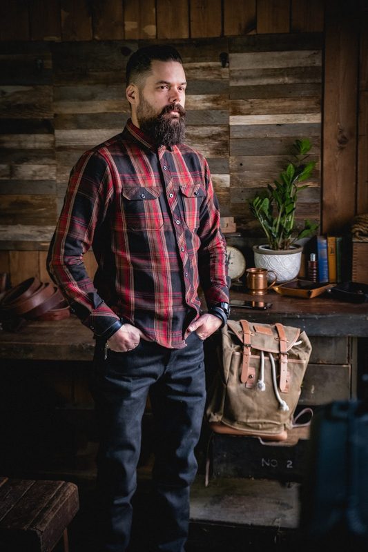 Man in a red flannel shirt in a workshop with a canvas pack
