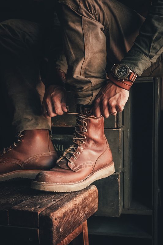 Lacing tall brown leather boots on a wooden stool