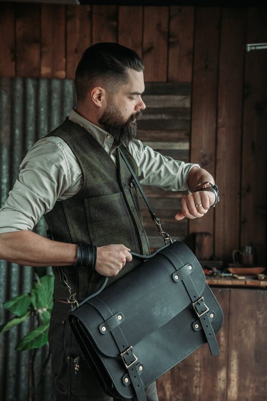 Man in a waxed vest checking his watch, black leather briefcase in hand