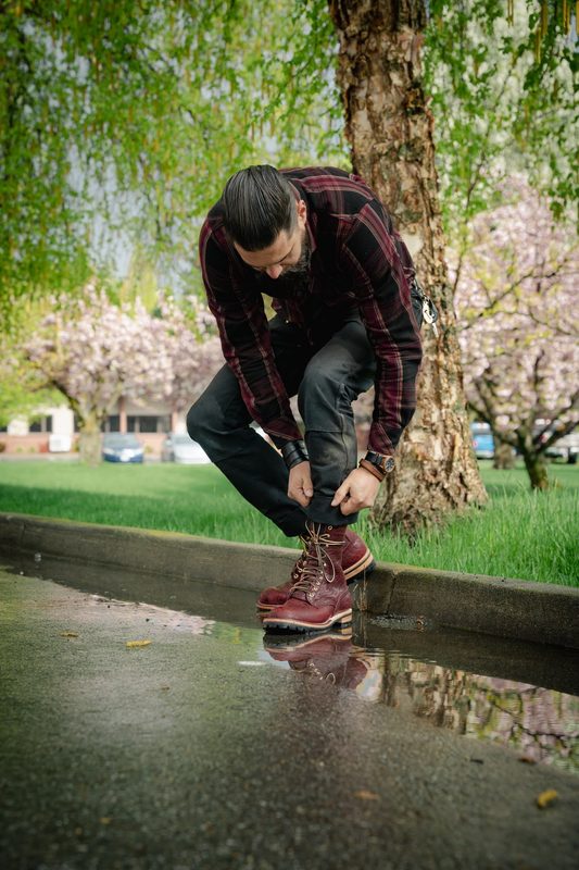 Man lacing oxblood boots beside a rain puddle