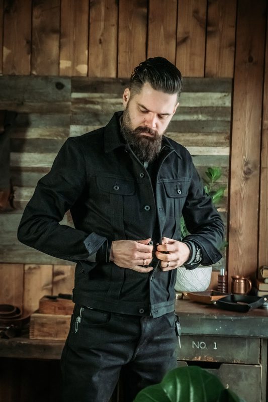 Man buttoning a black jacket in a wood-paneled room