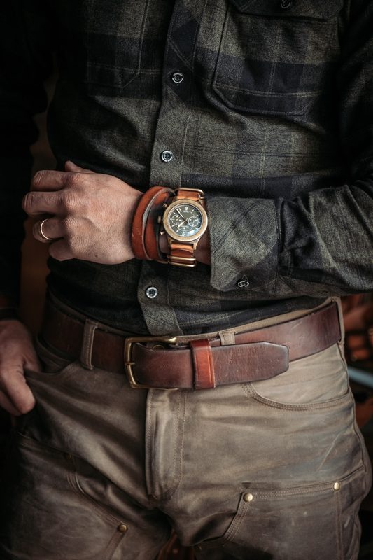 Bronze watch on a leather cuff and a brown belt over flannel