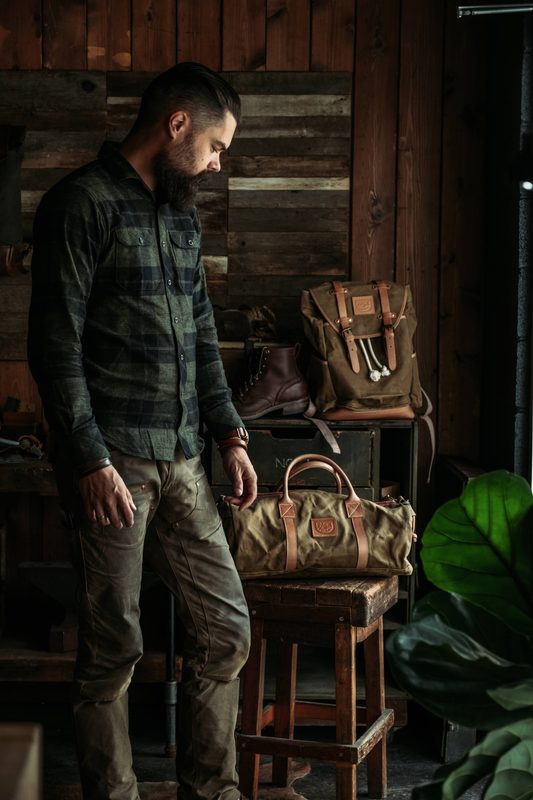 Man in flannel in a workshop with leather bags