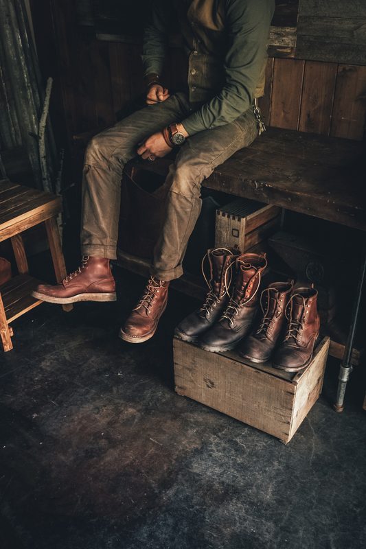 Seated man in work boots beside a crate of boots in a workshop