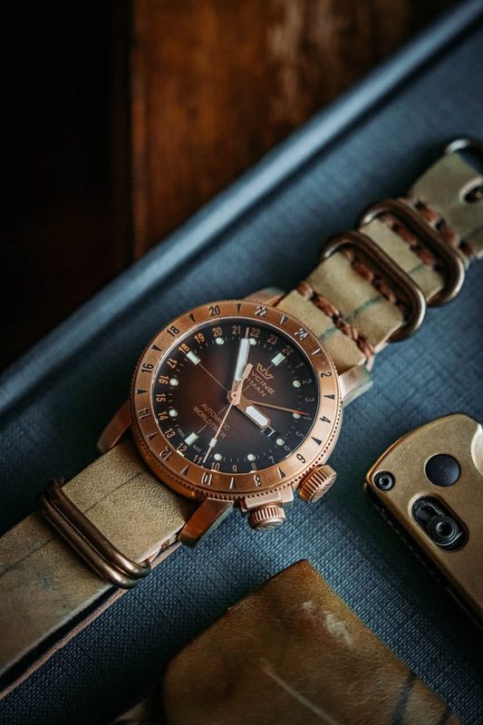 Bronze dive watch on a canvas strap beside a knife and cordovan leather goods