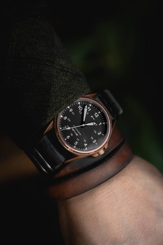 Bronze watch on a black strap with a leather wrist cuff in low light