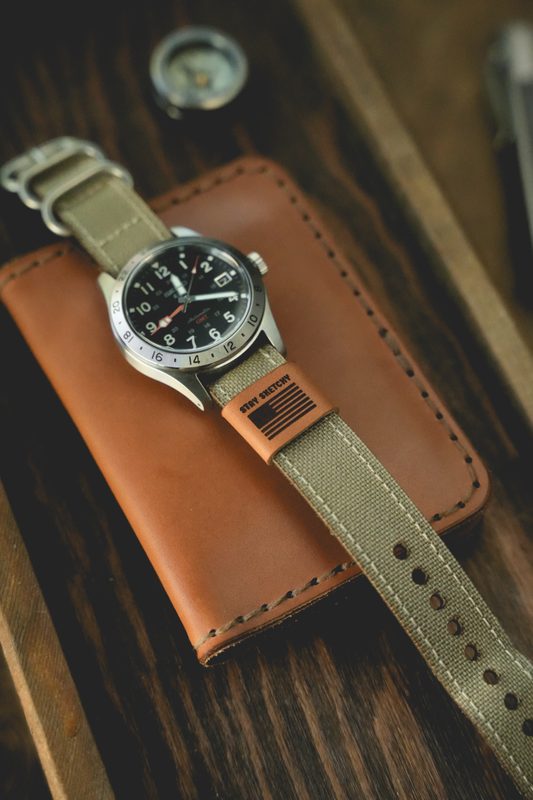 Steel field watch on an olive strap over a tan leather sleeve