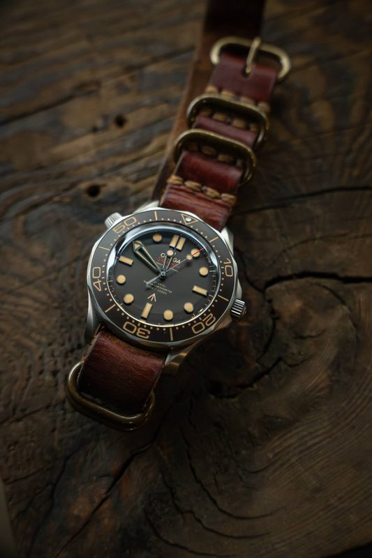 Dive watch on a brown leather NATO strap on a weathered plank