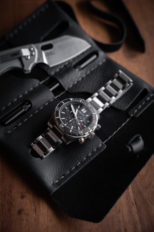 Steel chronograph on a bracelet in a black leather roll with a folding knife
