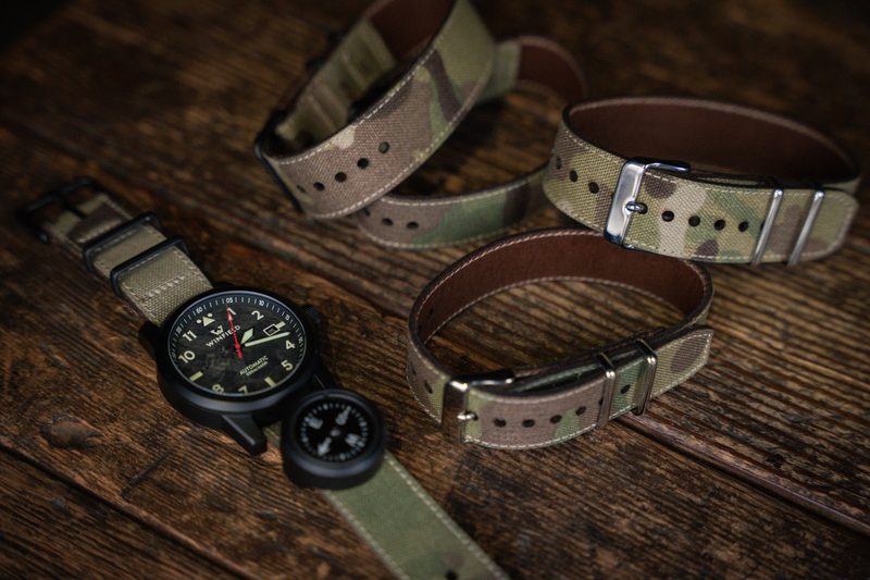 Black watch and compass with a set of camo and canvas straps on wood