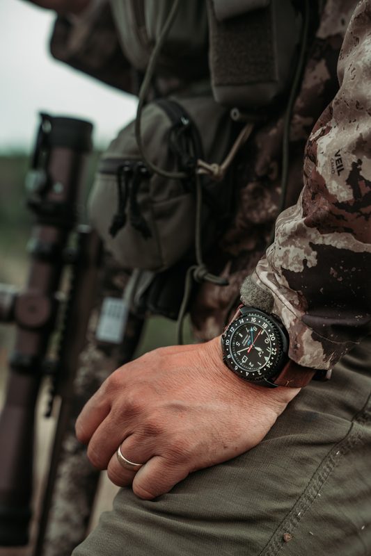 Field watch on the wrist at elk camp, rifle and camo in the background