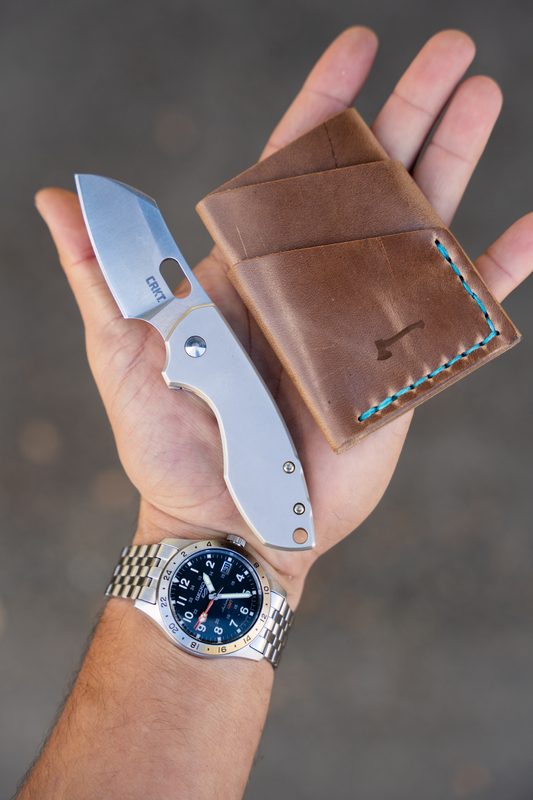 Open hand holding a leather wallet and folding knife, steel watch on the wrist